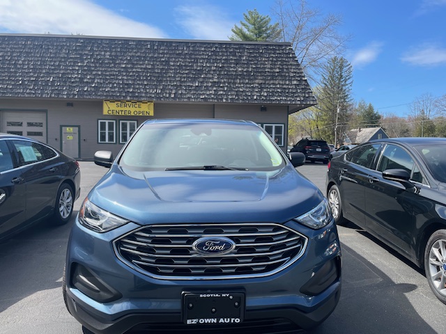 Front view of a blue Ford SUV parked in a dealership lot with a service center building in the background and a 'Service Center Open' sign behind it.