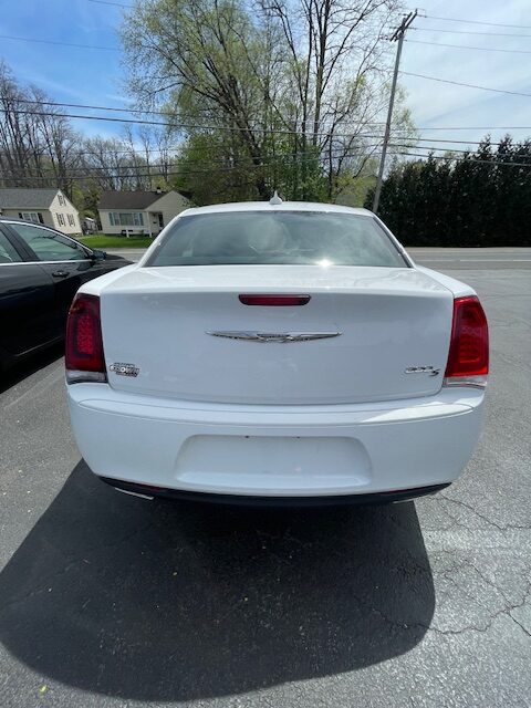 Rear view of a white Chrysler 300 sedan parked in a lot, showing red taillights, chrome emblem on the trunk, and the '300' badge on the right side.