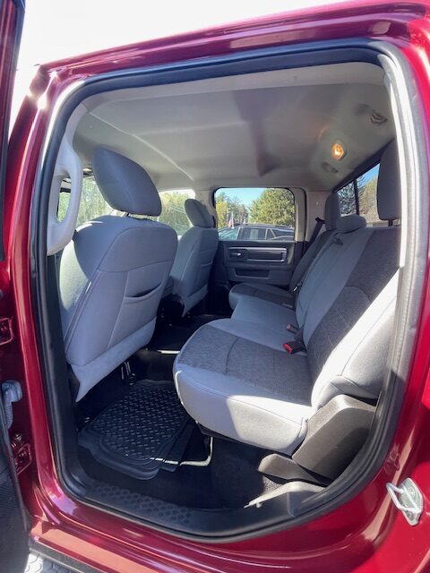 Red pickup truck interior: back seat with gray cloth upholstery and three seat belts, view from open rear door on sunny day