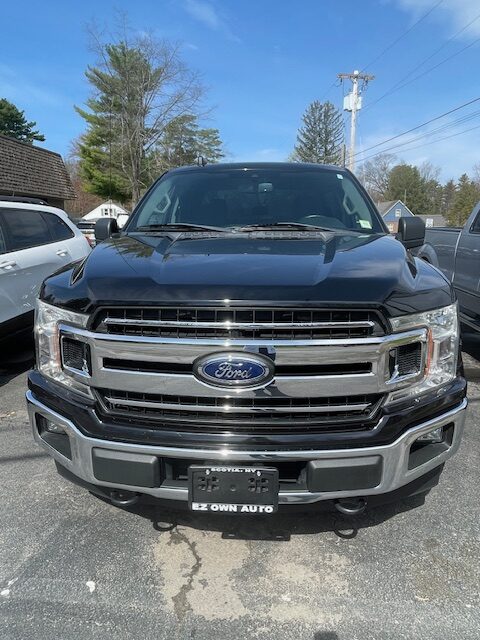 Front view of a dark blue Ford pickup truck parked in a lot, chrome grille with Ford emblem and rectangular headlights.