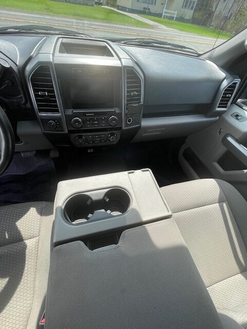 Interior of a pickup truck cabin: front dashboard with central touchscreen and climate controls, and a fold-down center armrest with two cup holders.