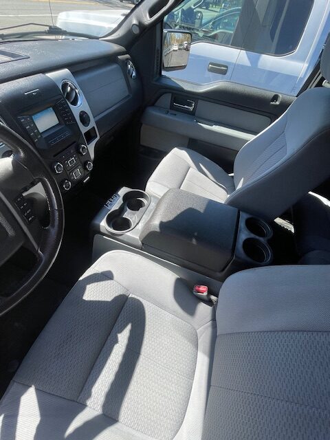Front interior of a pickup truck showing the steering wheel, dashboard controls, and gray fabric seats with a center console featuring cup holders.