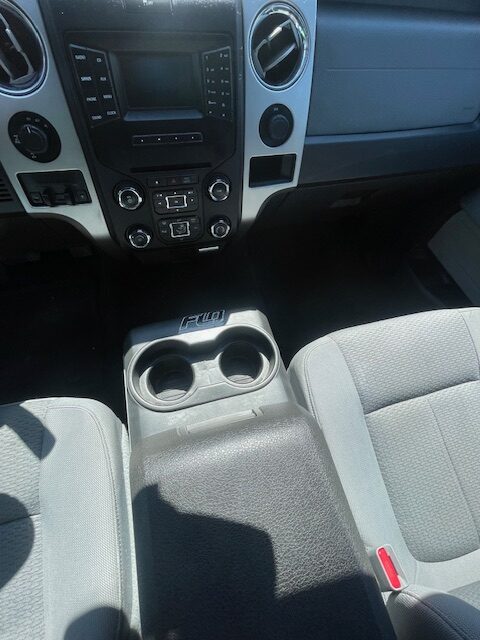 Front seat area of a pickup truck interior: center stack with radio and climate controls, and two cup holders in the center console.