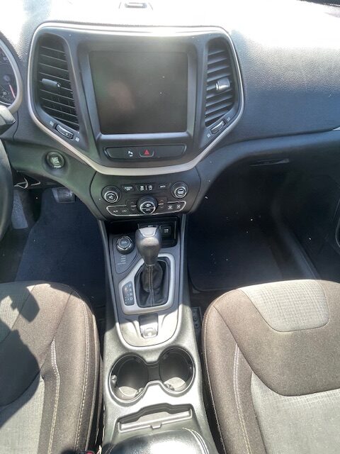 Center console in a car: touchscreen display framed by vents, climate controls, and gear shifter with cupholders visible below.