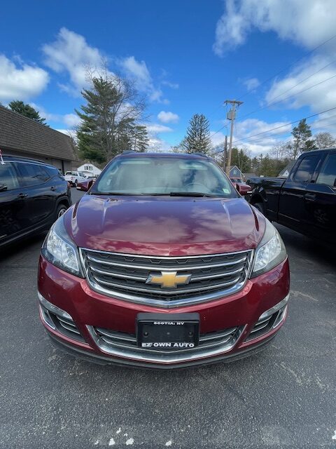 Front view of a maroon Chevrolet SUV parked in a dealership lot, chrome grille with gold bowtie emblem and a black license plate frame reading EZ Own Auto.