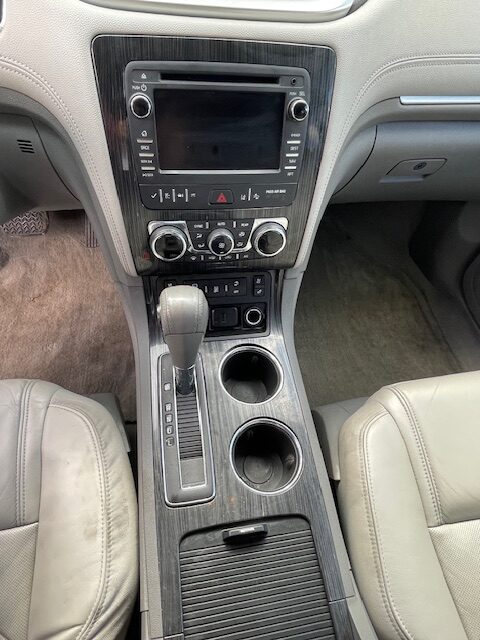 Center console of a car showing the gear shift, two cup holders, and an infotainment screen with climate controls surrounding it.
