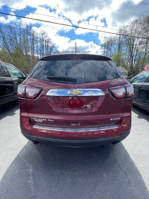 Rear view of a maroon Chevrolet Traverse AWD SUV parked in a lot; visible chrome bumper, taillights, and Chevy emblem on the tailgate.