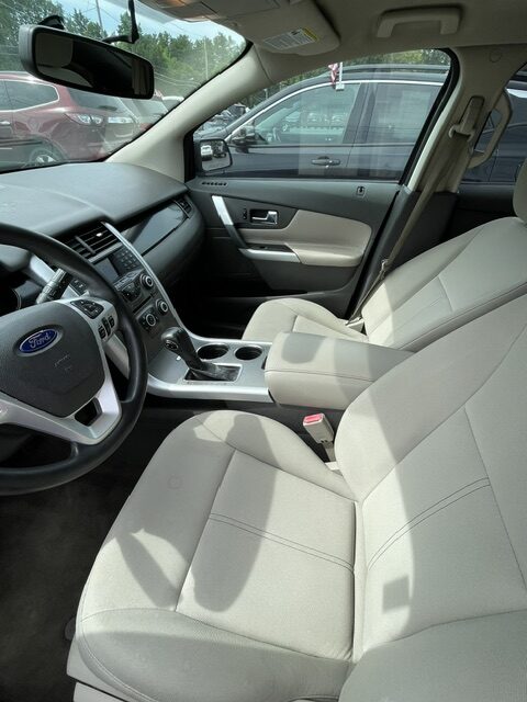 Front cabin of a beige Ford car: driver and passenger seats, center console, and steering wheel visible from the driver's seat.