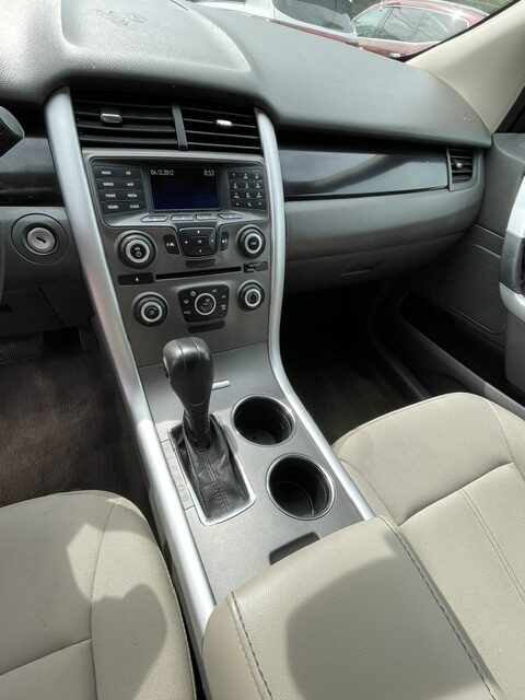 Interior of a car focusing on the center console: gear shift, two cup holders, and climate/infotainment controls in a silver trim area.