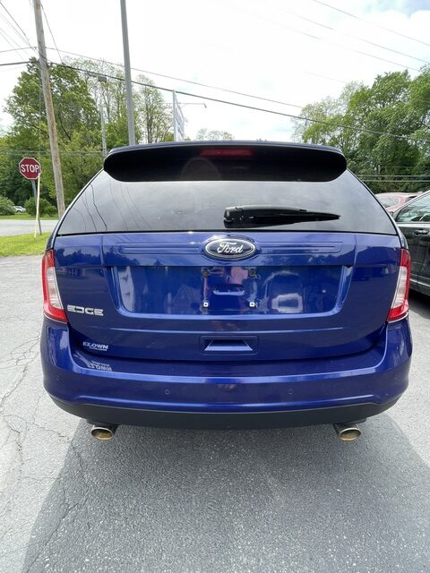 Rear view of a blue Ford Edge SUV parked in a lot, showing the tailgate, rear windshield wiper, and dual exhausts.