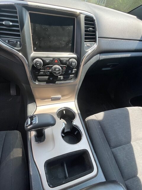 Inside a car cabin showing the center console: touchscreen display, climate and media controls, gear shifter, two cup holders, and a storage pocket.