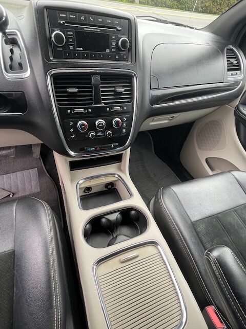 Center console of a car interior with a touchscreen stereo, climate controls, and cup holders visible between leather seats on a light-beige console panel.