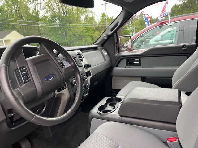 Front interior of a gray pickup truck, showing steering wheel, dashboard, center console with cup holders, and driver seat edge