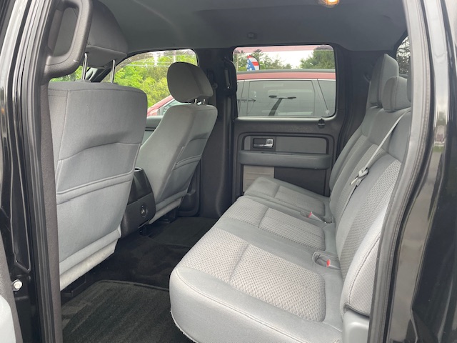 Interior of a black crew cab vehicle showing gray cloth rear bench seat with three seat belts and headrests, front seats visible.