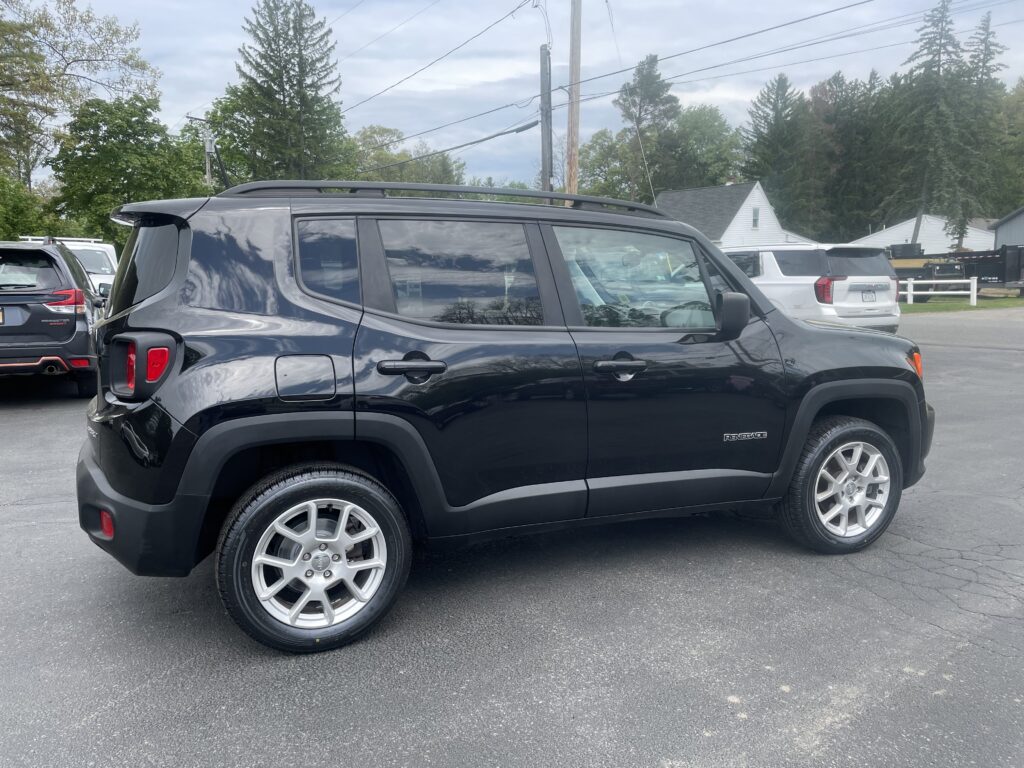 Black Jeep Renegade SUV parked in a lot with other vehicles and trees in the background, utility poles and power lines overhead.