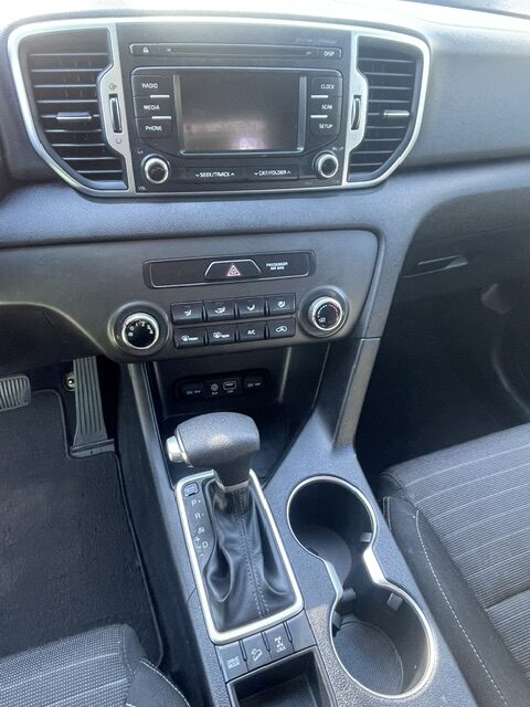 Car interior center console with touchscreen infotainment, climate controls, gear shifter, and two cup holders
