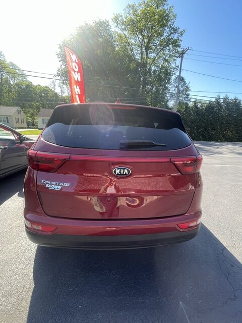 Rear view of a red Kia Sportage SUV parked in a lot, showing the Kia badge and Sportage trim, with a red banner in the background.