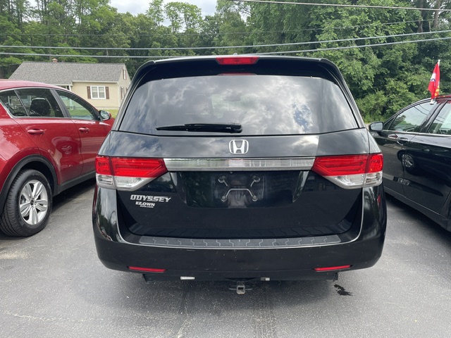 Rear view of a black Honda Odyssey minivan in a parking lot, no license plate visible, with red and black cars on either side.