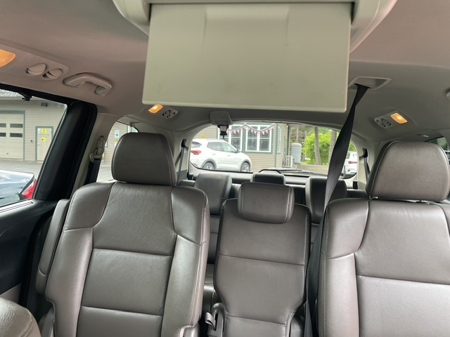 Interior of an SUV with a folded-down overhead entertainment screen and leather seats; view of parked cars through the windows.