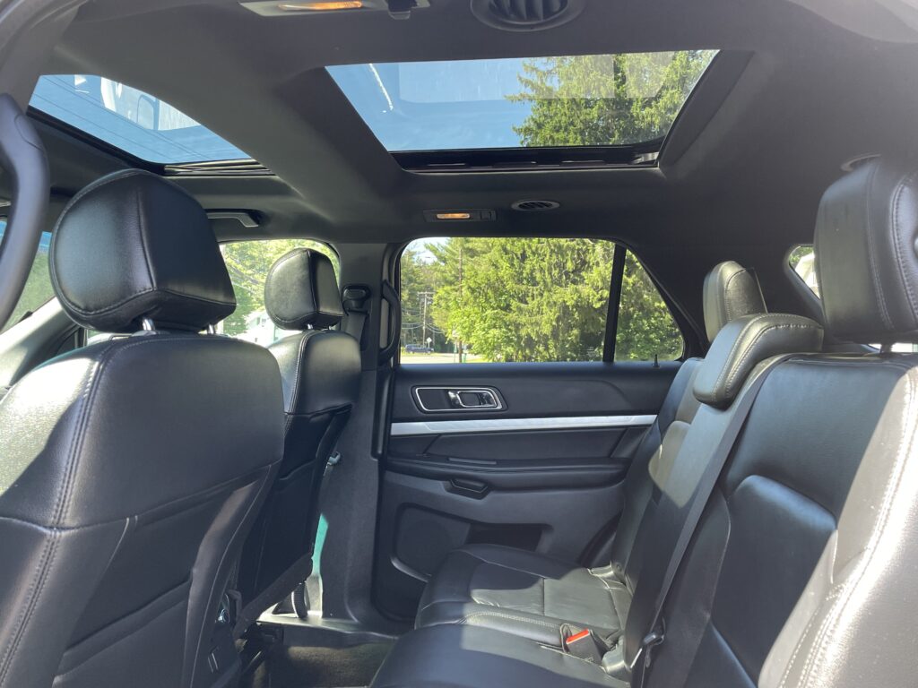 Interior of a black leather SUV showing the rear seats with headrests and a panoramic sunroof above.