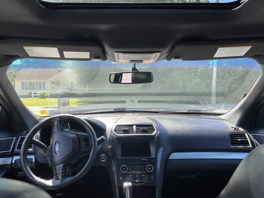 Front interior of a Ford car showing steering wheel, center console, and rearview mirror with sun visors up in a parked vehicle