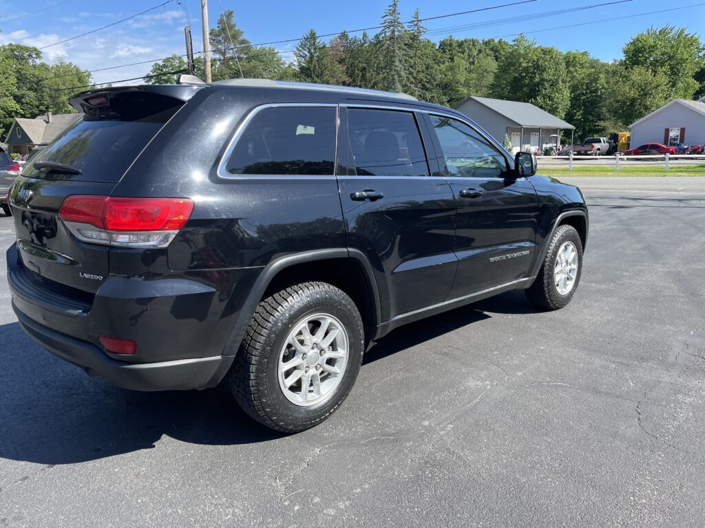 Black SUV parked in a parking lot, showing the rear and passenger side with a visible Grand Cherokee badge and Laredo trim.