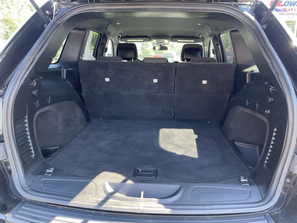 Open SUV cargo area with third-row seats folded, revealing a spacious black carpeted trunk.