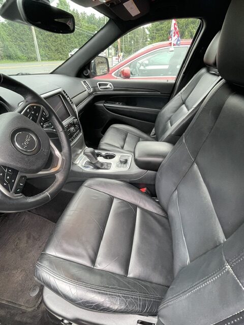 Leather-clad front seats and steering wheel of a Jeep, with a center console and dashboard visible inside the car.