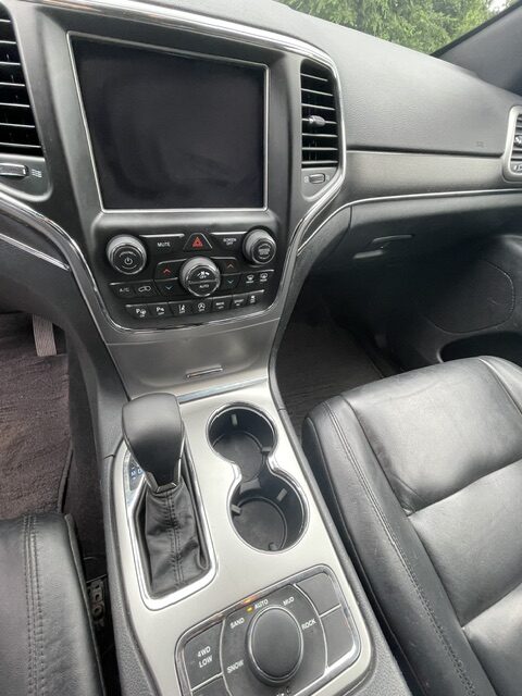 Center console inside a car: gear shifter, two cup holders, and a large touchscreen infotainment display with climate controls.
