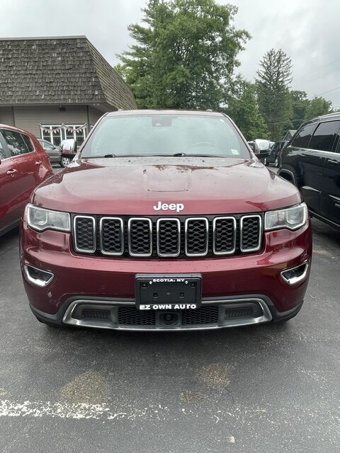 Front view of a red Jeep Grand Cherokee in a dealership lot, showing the seven-slot grille.